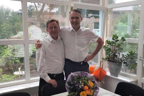 Frank Wissing Arm in Arm mit Thorsten Friedrich mit Blumenstrauß zum 10-jährigen Jubiläum bei der WiR Solutions im Vordergrund