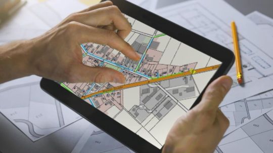 Tablet, auf dem eine Hand an ein Beispielbild zur Netzplanung mit verschiedenen Straßenzügen zu sehen ist