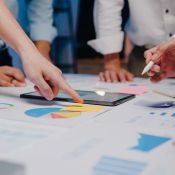 Menschen stehen um einen Tisch mit Grafiken und einem Tablet und zeigen darauf