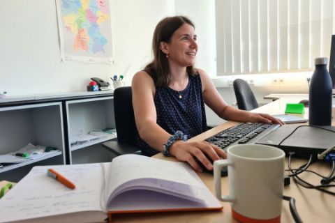 Praktikantin Liv, die am PC arbeitet. WiR Notizbuch und Kaffeetasse im Vordergrund