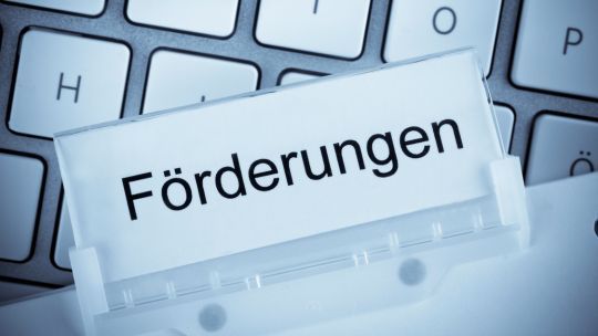 Ein Karteikartenreiter mit dem Wort ‚Förderungen‘ steht vor einer Computer-Tastatur.