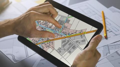 Tablet, auf dem eine Hand an ein Beispielbild zur Netzplanung mit verschiedenen Straßenzügen zu sehen ist