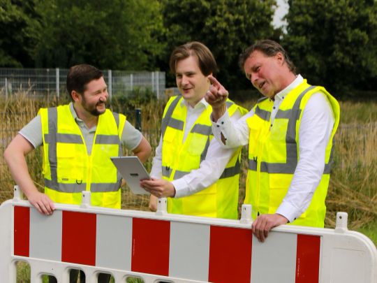 Drei Mitarbeiter der WiR Solutions stehen mit gelben Warnwesten vor einem Bauzaun. Einer hat ein Tablet in der Hand