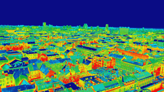 Das Bild zeigt eine thermografische Ansicht einer Stadtlandschaft im Kontext der kommunalen Wärmeplanung. Die unterschiedlichen Farben markieren Temperaturunterschiede in den Gebäuden und Straßen: warme Bereiche erscheinen in Rot- und Gelbtönen, während kühlere Bereiche in Grün- und Blautönen dargestellt sind. Der dunkle blaue Himmel im Hintergrund signalisiert niedrigere Temperaturen. Diese Darstellung hilft bei der Identifizierung von Wärmeverlusten und ist ein wichtiges Werkzeug zur Verbesserung der Energieeffizienz in städtischen Gebieten.