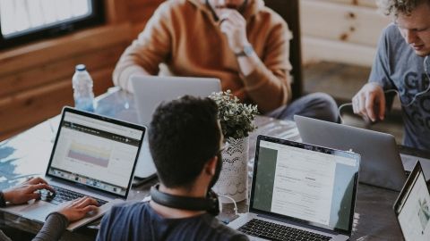 Vier Männer mit Laptops sitzen um einen Tisch und arbeiten