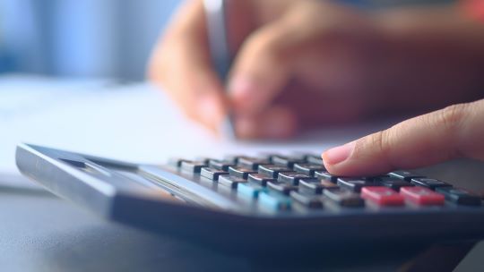 Person bedient Taschenrechner und schreibt auf Papier