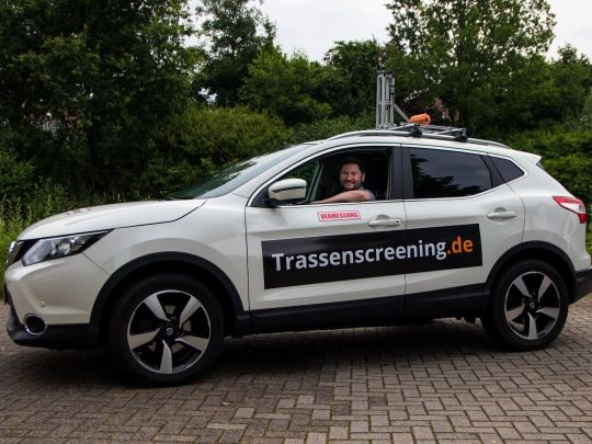 Mitarbeiter der WiR Solutions im weißen Trassenscreening-Auto mit der Aufschrift trassenscreening.de und Kamerainstallation auf dem Dach