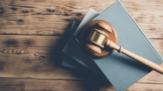 Holztisch von oben, auf dem drei übereinandergestapelte Bücher und darauf ein Holzhammer liegen