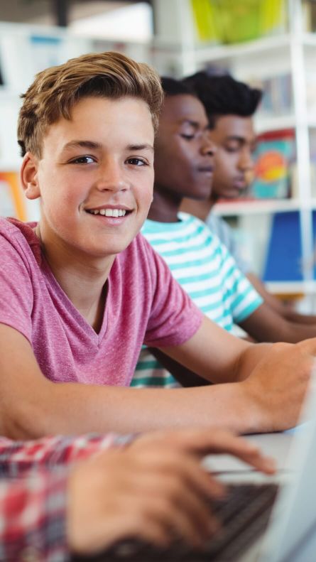Zu sehen sind drei Kinder mit Laptops. Ein Junge lächelt in die Kamera.